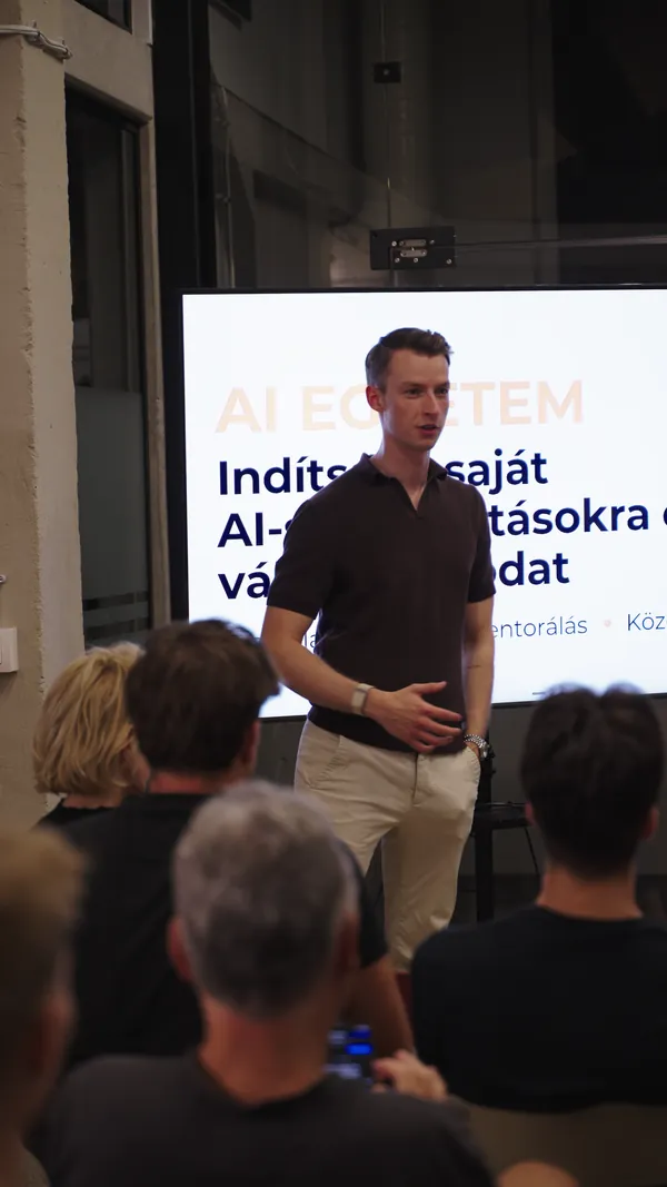 Előadó gesztikulálva mesél az AI Egyetem vállalkozásindító képzéséről a kivetített dia előtt.